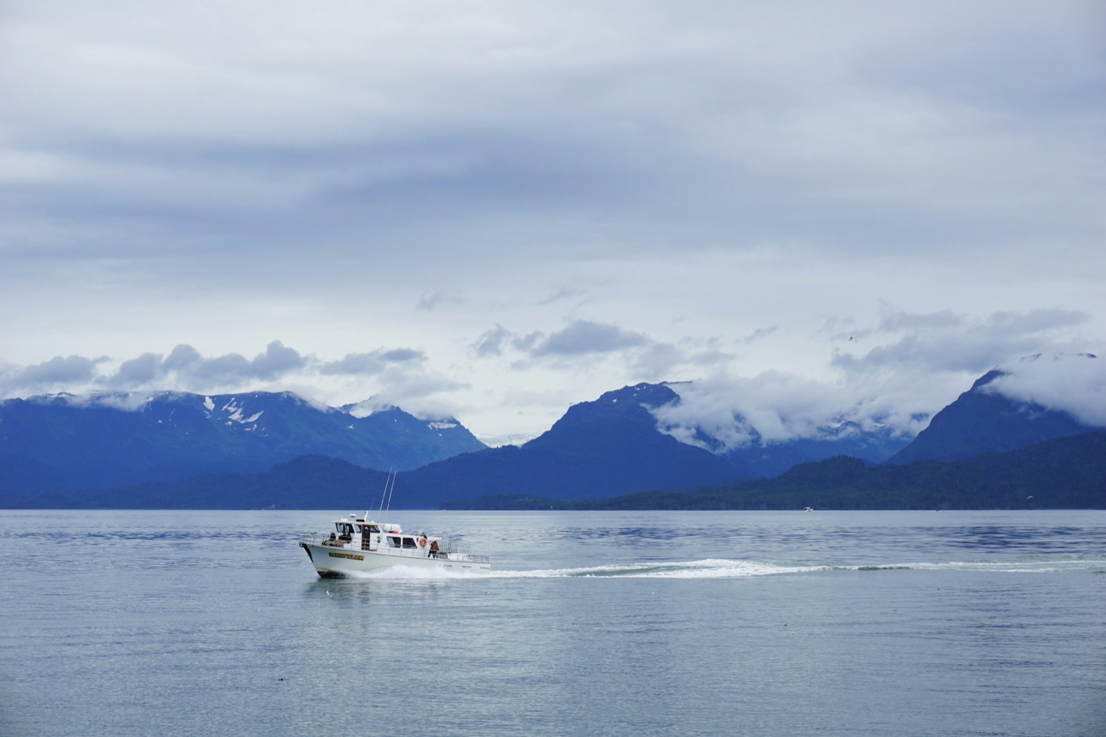 Charter boat running beneath cloud-covered coastal mountains