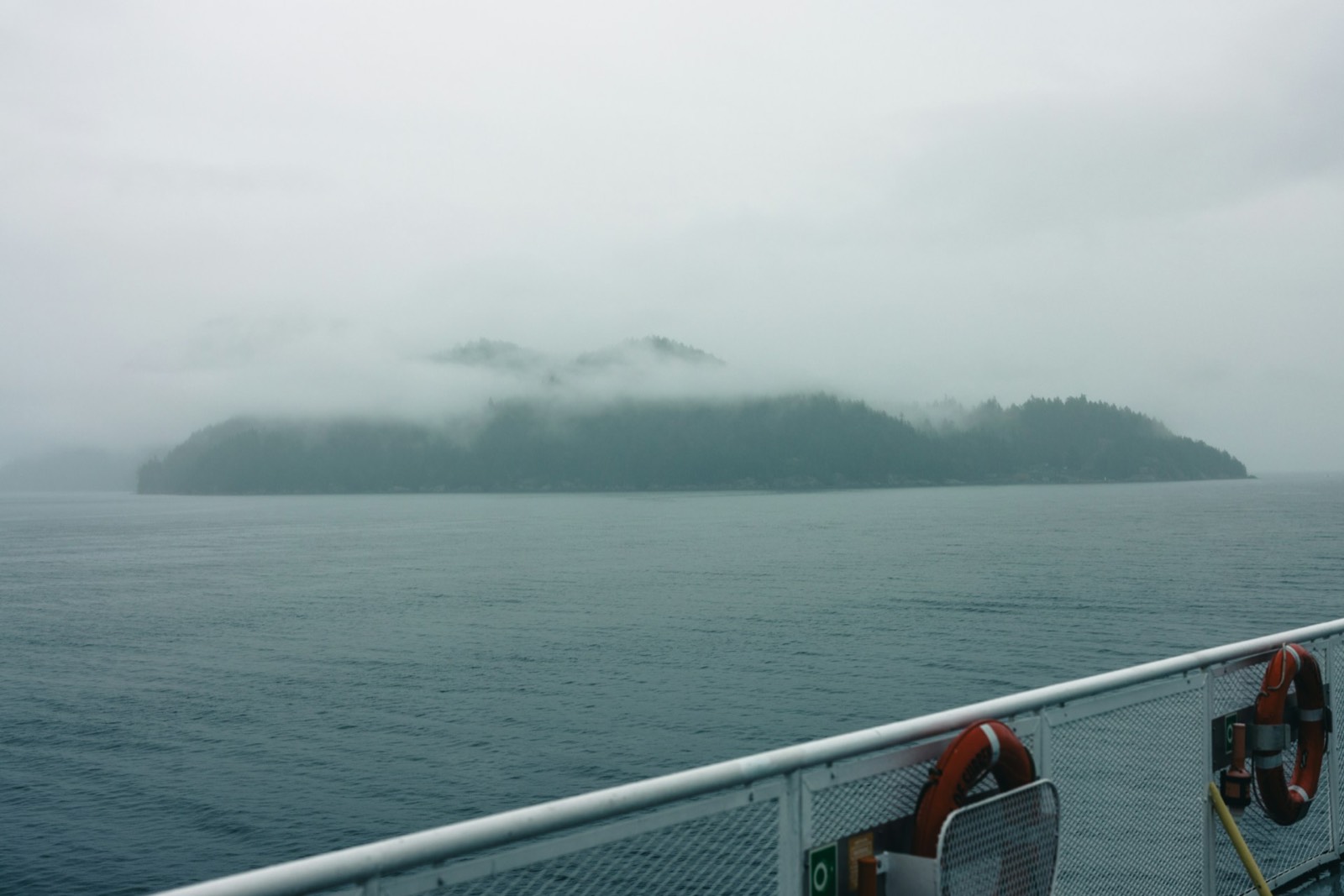 Forested island wrapped in fog seen from a boat deck